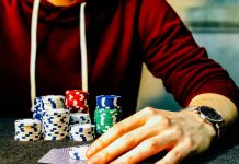 person holding playing cards beside poker chips