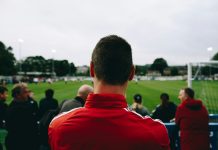 man standing while watching soccer during daytime