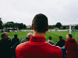 man standing while watching soccer during daytime