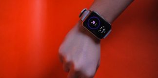 Fist wearing a smartwatch with fitness tracking display on a vibrant orange background.
